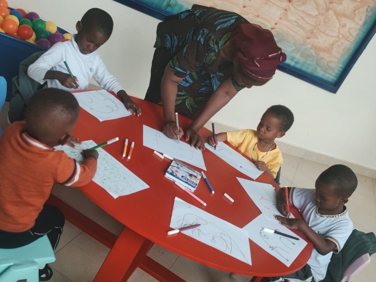 Children drawing with markers at a red table